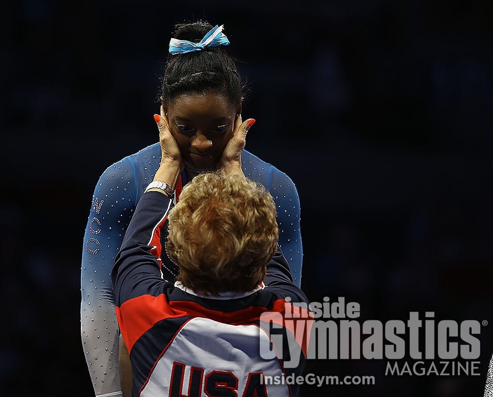 An Inside Gymnastics photograph of Martha Karolyi cupping Simone Biles's face in both hands after a routine.