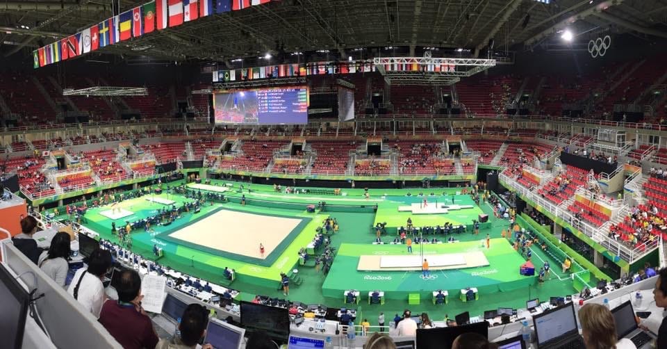 The Rio arena from high in the press tribune during qualification: floor, bars and vault laid out on the green podium, national flags hanging from the roof.