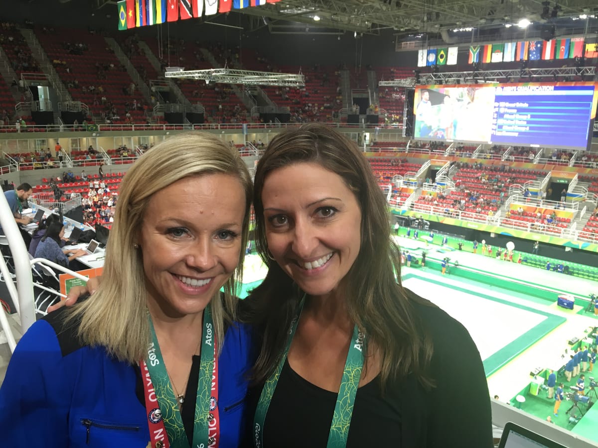 Gina Pongetti Angeletti and a colleague in the arena stands, the competition floor and scoreboard below them.