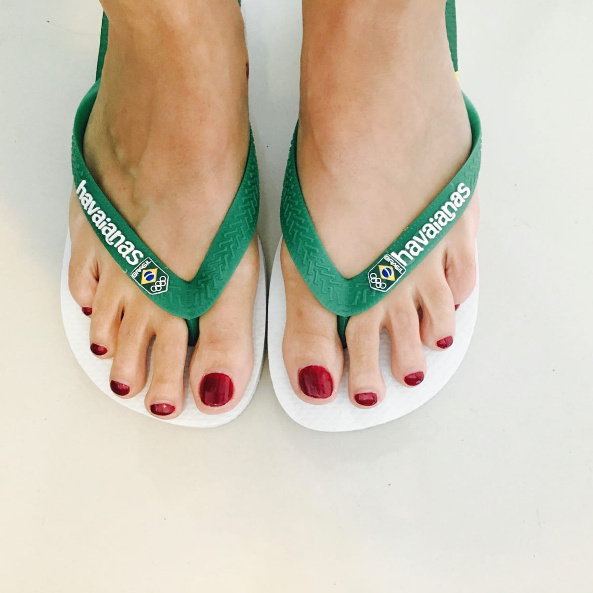 A pair of feet in green and white Havaianas carrying the Brasil Olympic crest, photographed from above.