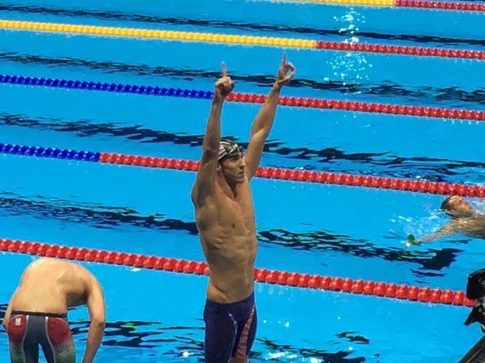 Michael Phelps standing in the pool after a race with both index fingers raised.
