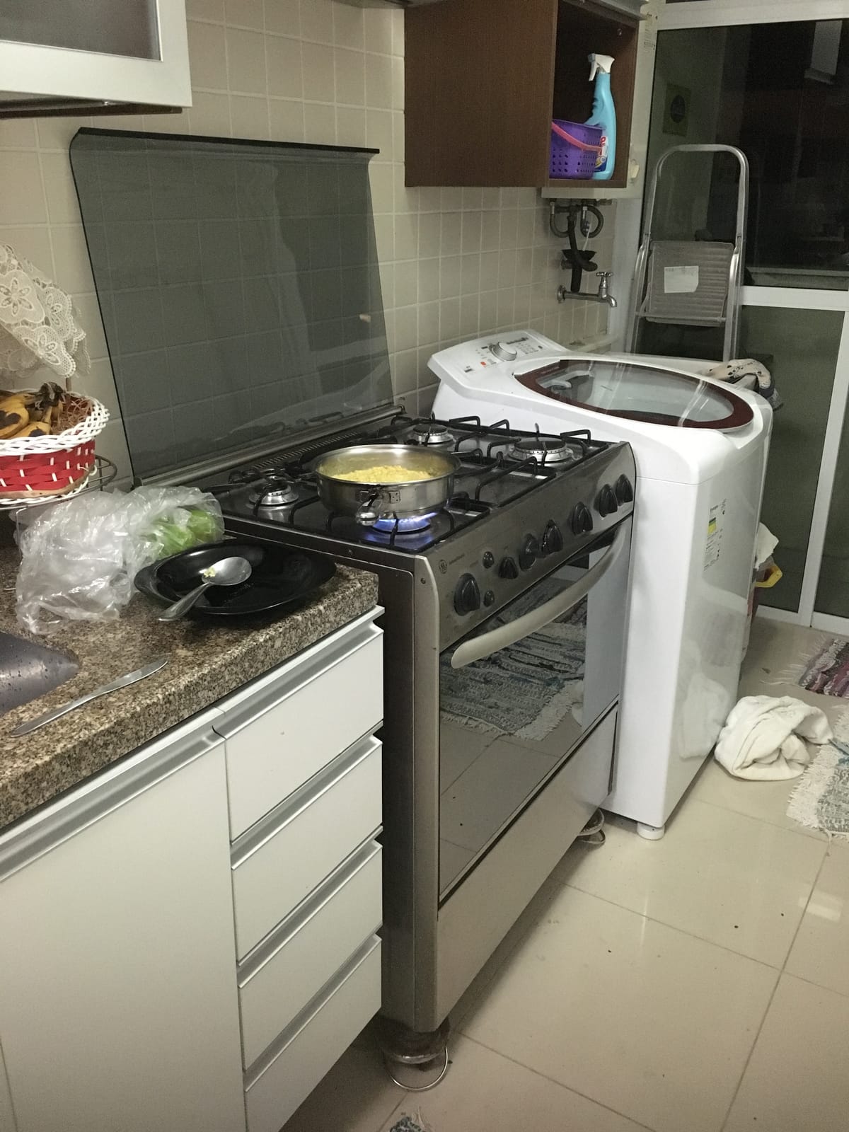 A small Brazilian apartment kitchen with a pan of food on the gas range and a washing machine standing directly beside the cooker.