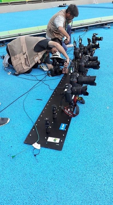 Two photographers crouched on the blue athletics track rigging a long row of remote cameras bolted to a rail.