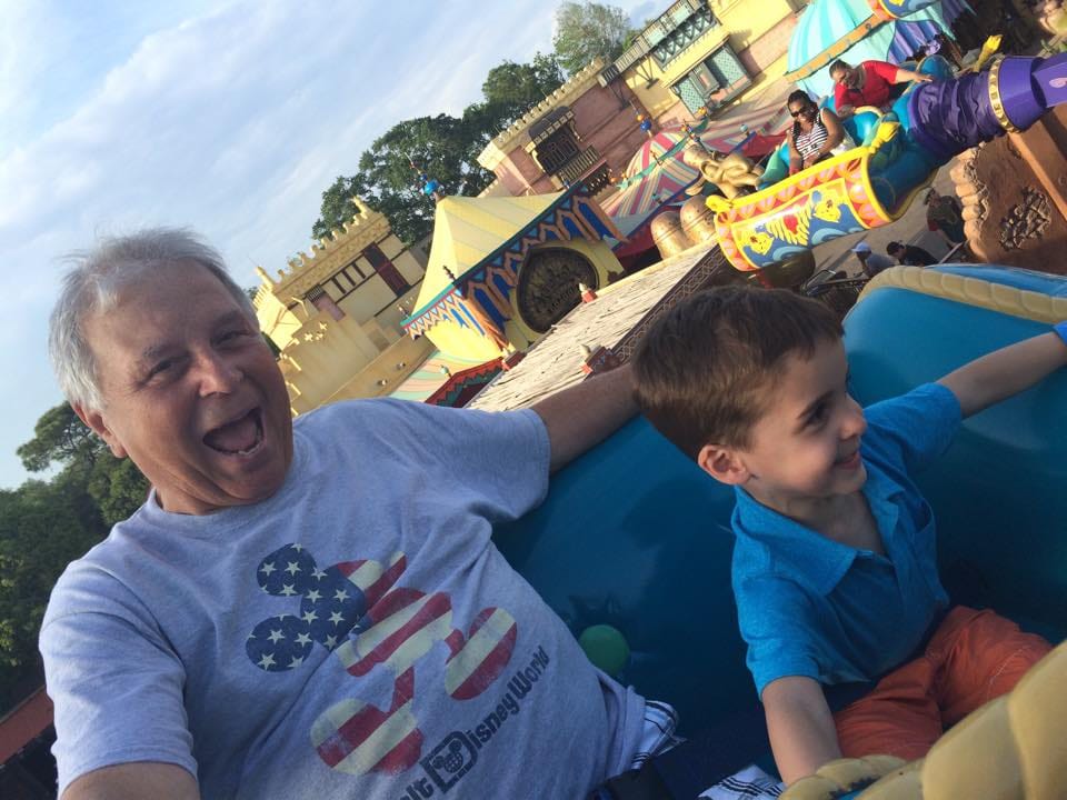 Gina's father laughing beside her young son on a fairground ride, both mid-grin.