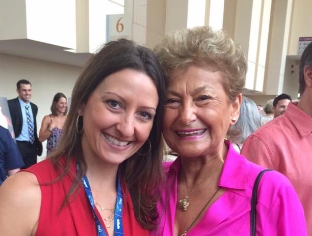 Gina Pongetti Angeletti cheek to cheek with Martha Karolyi in a bright pink blouse at a crowded indoor event.