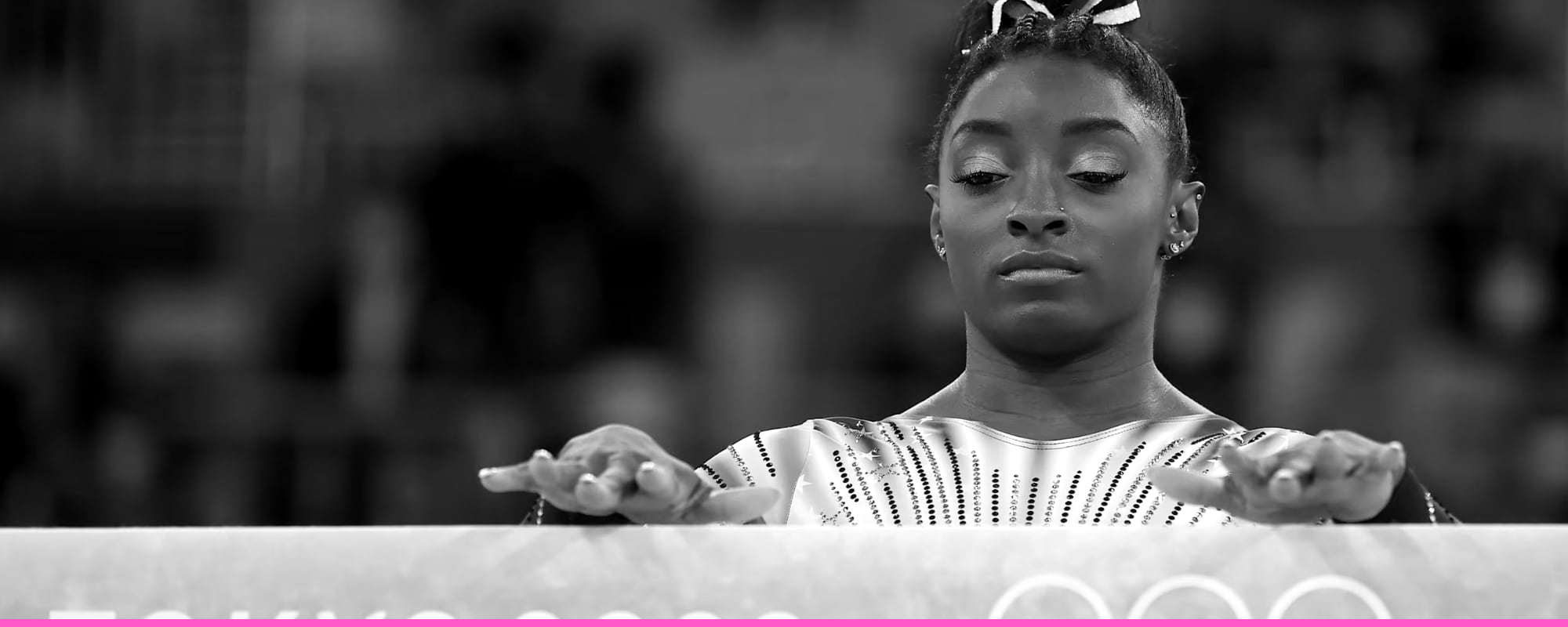 Simone Biles standing at the balance beam in Tokyo, hands resting on it, looking down and composing herself.